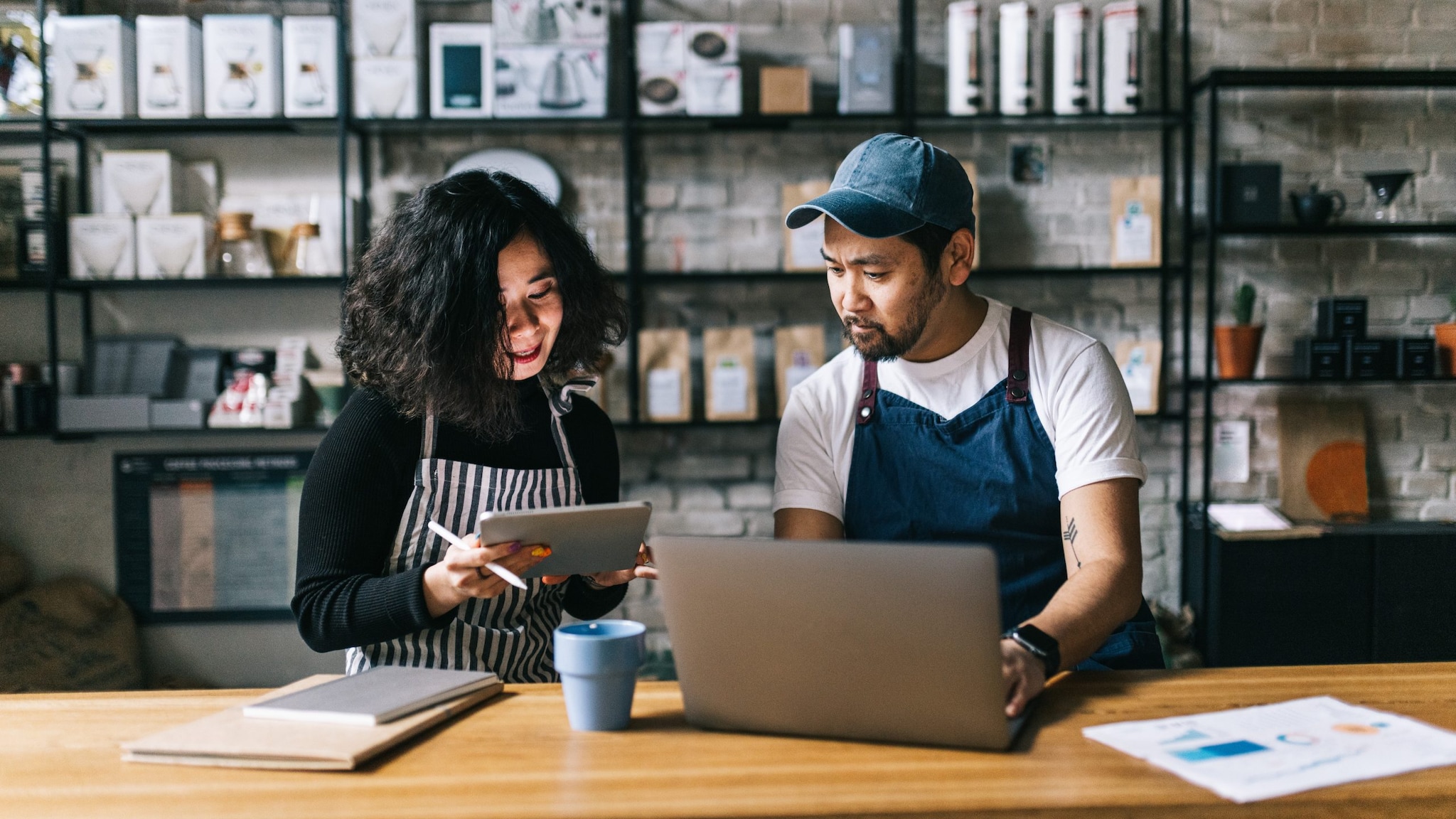 two people sitting in front of a table with a laptop and notebook